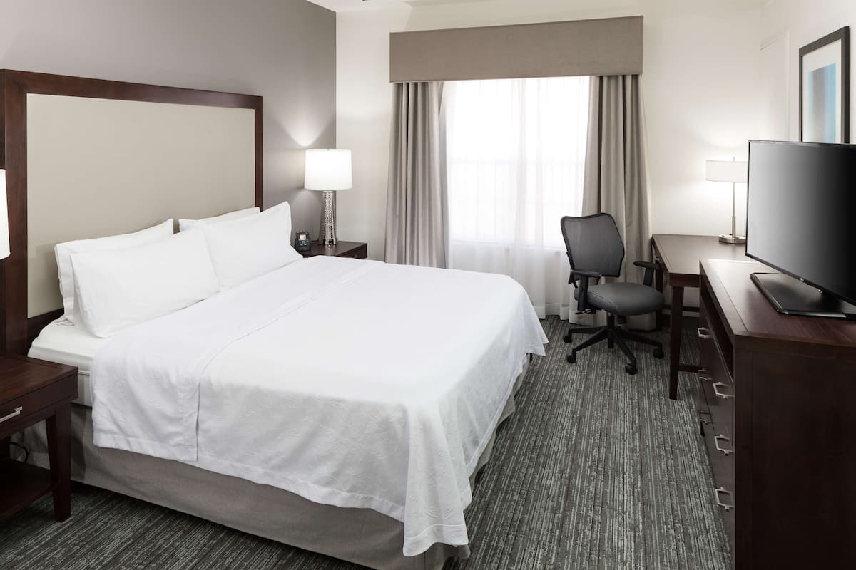 A hotel room with a large bed, a desk with a chair, a television, and a window with curtains.