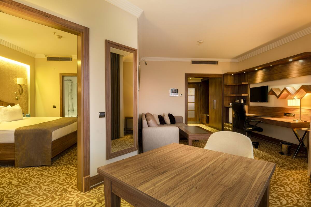 A hotel room with a bed, a sofa, a desk, a chair, a TV, and a mirror.