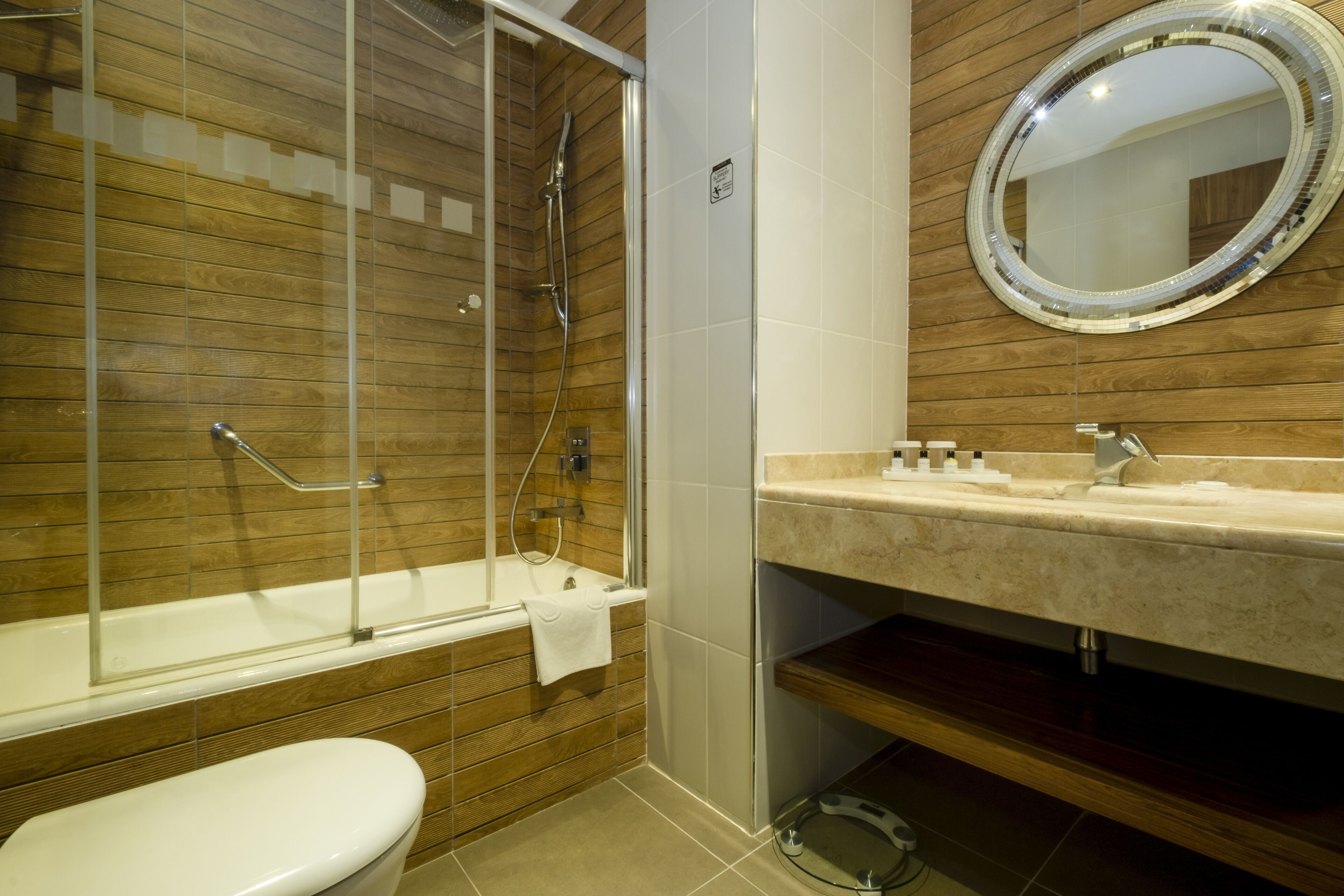 Un bagno moderno con parete in legno, box doccia in vetro, water bianca e lavabo in marmo con specchio sopra.