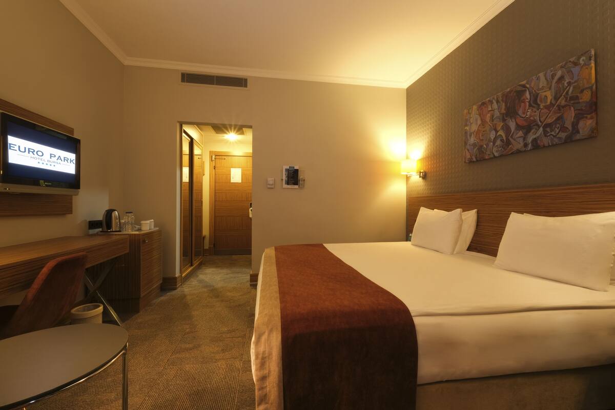 A hotel room with a bed, a desk with a chair, a television, and a painting on the wall.