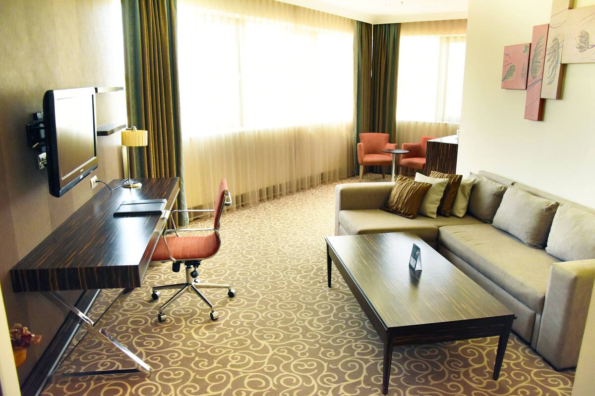 A hotel room with a sofa, a coffee table, a TV, a desk, and a chair.