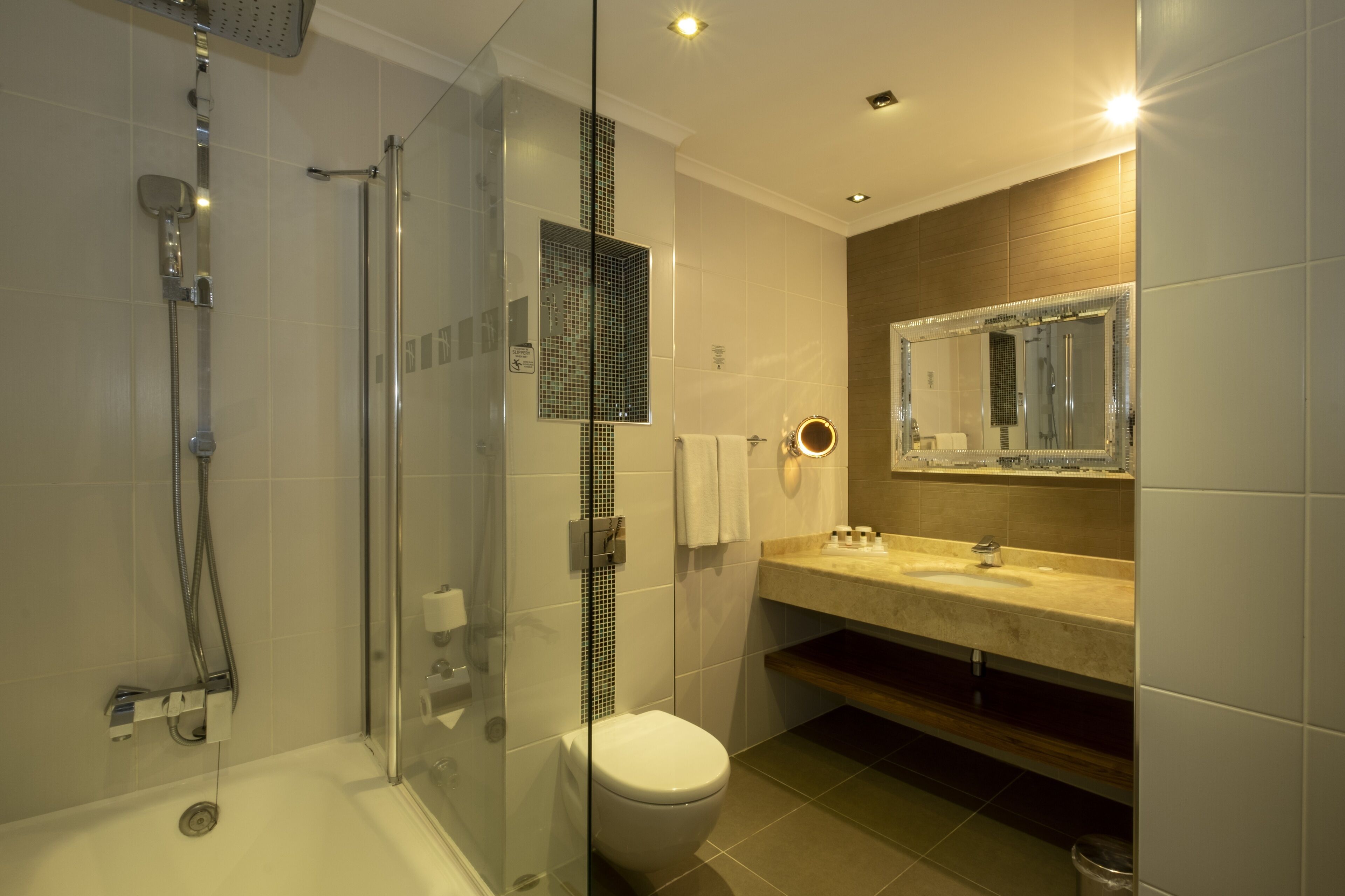 Un baño moderno con cabina de ducha de vidrio, inodoro y tocador con espejo.