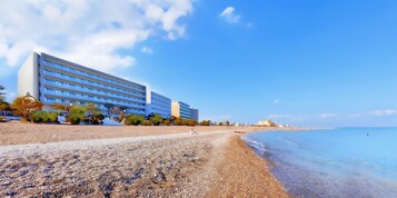 Un hotel mediterráneo con vista a la playa, una playa de guijarros y aguas cristalinas.