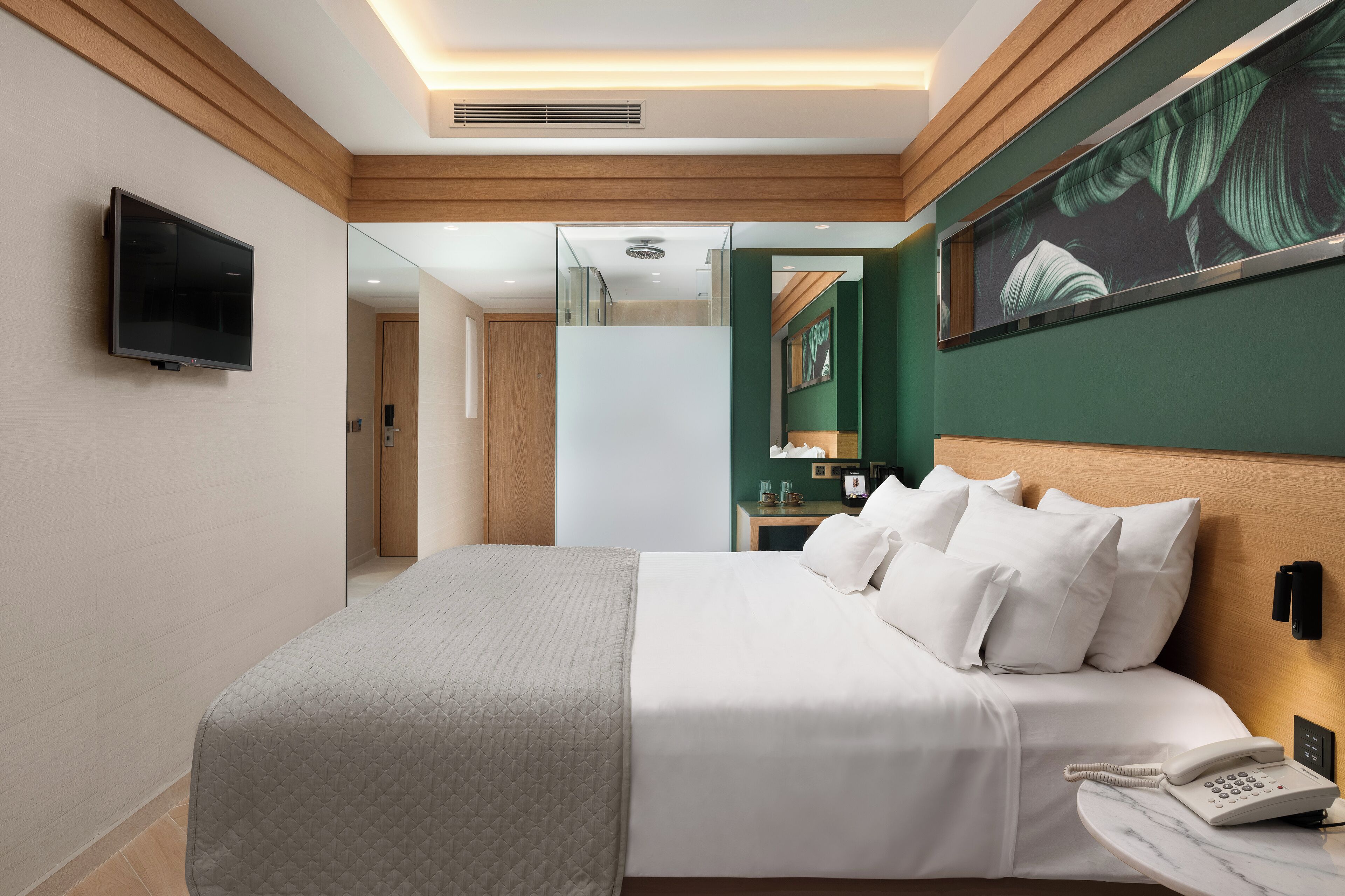 A modern hotel room with a large bed, a mounted TV, a bedside phone, and a green accent wall.