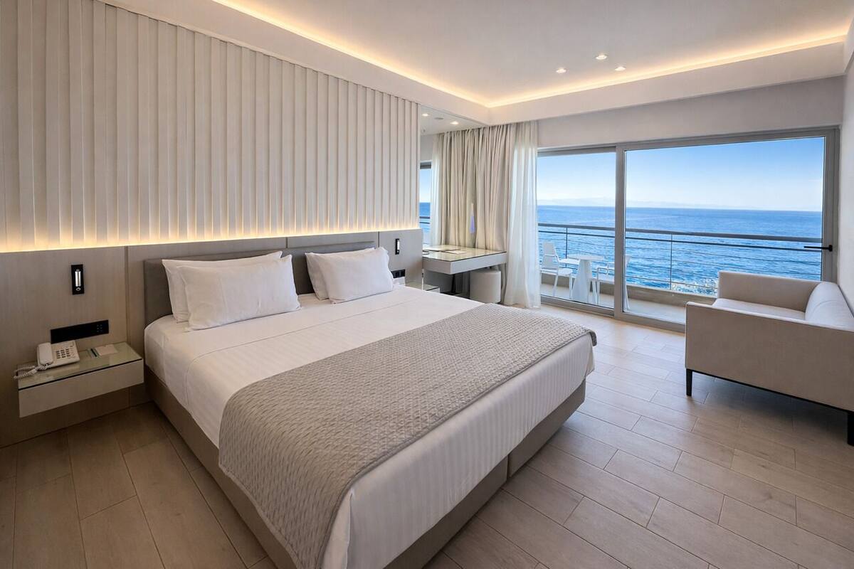 A modern hotel room with a large bed, a desk, and a view of the ocean.