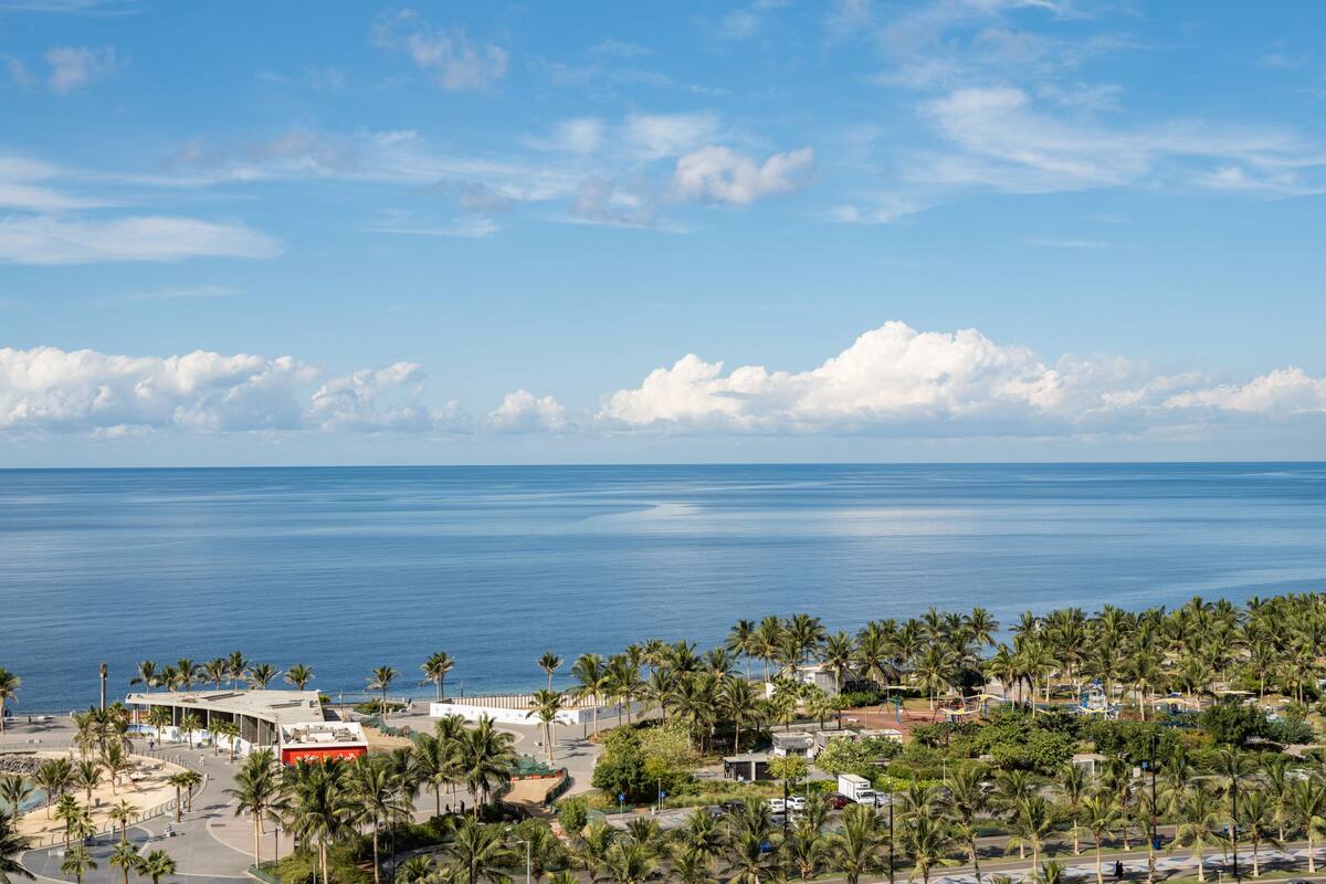 A coastal cityscape with a view of the sea, palm trees, and buildings.