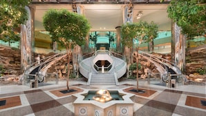 Un lobby espacioso con una fuente central, varias escaleras y abundante vegetación.