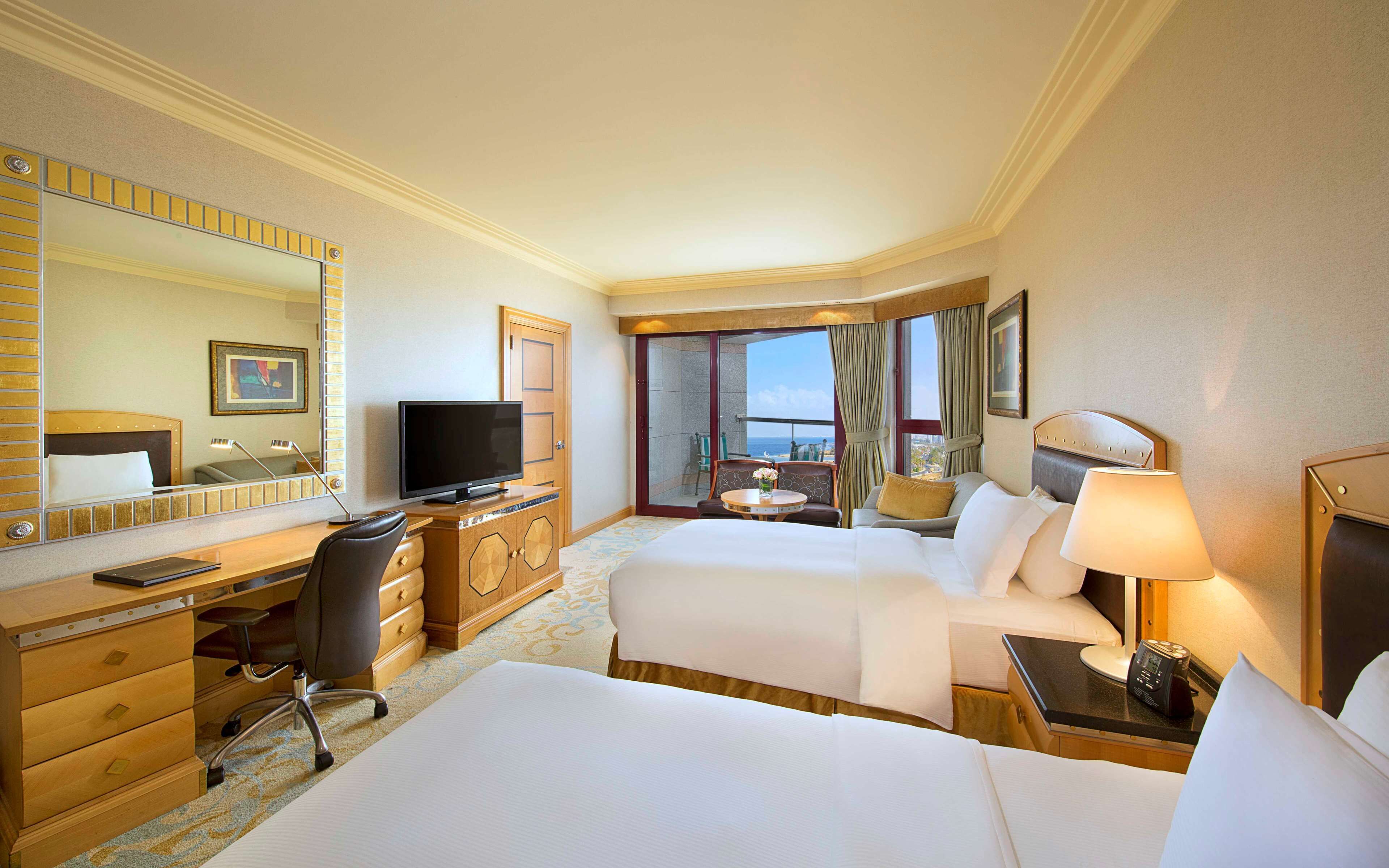 Habitación de hotel con dos camas, un escritorio, un televisor, una silla y vista al océano.
