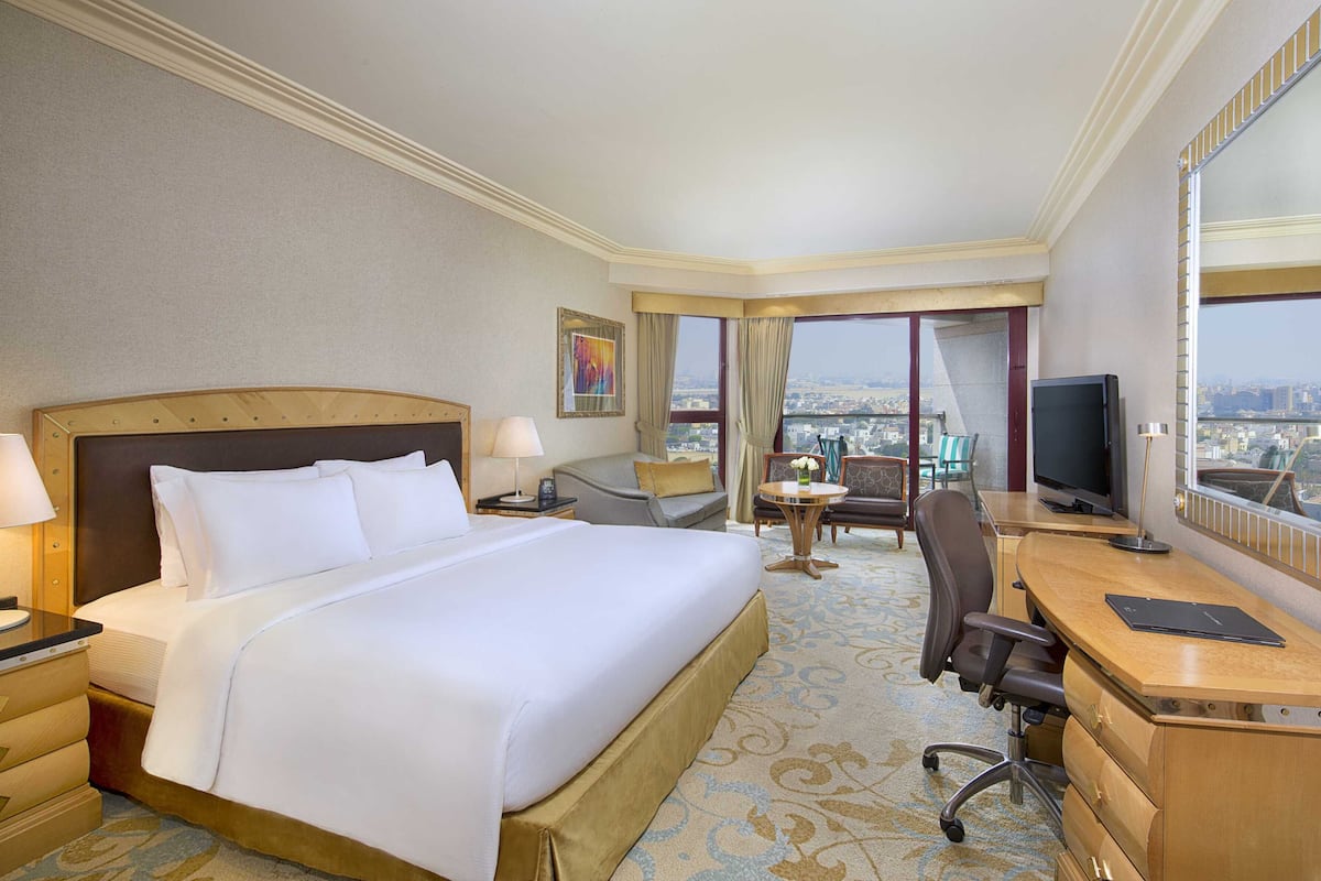 A hotel room with a large bed, a desk with a laptop, a TV, and a view of the city.