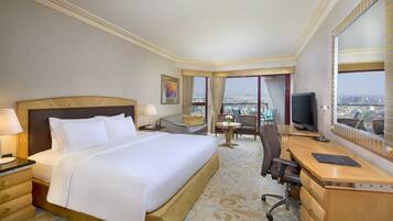 Ein Hotelzimmer mit einem großen Bett, einem Schreibtisch mit einem Laptop, einem Fernseher und Blick auf die Stadt.