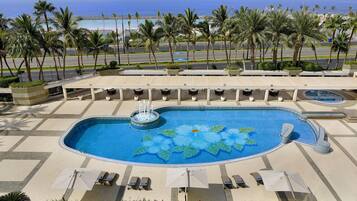 A swimming pool with a fountain, surrounded by lounge chairs and umbrellas, with a view of the ocean and palm trees.