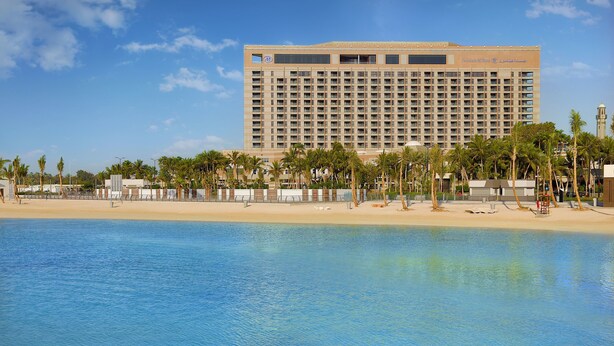 Un hotel grande con vista a la playa, palmeras y una piscina azul cristalina.