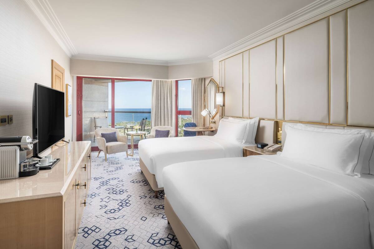 A hotel room with a bed, a desk, a TV, and a view of the ocean.