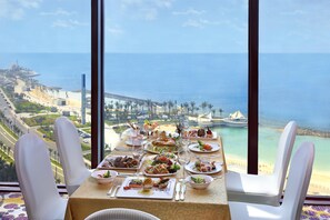 Une table dressée pour un repas, avec vue sur l’océan et sur le paysage urbain de la côte.