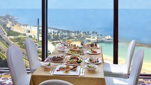 Una mesa dispuesta para una comida, con vistas al océano y al paisaje urbano costero.