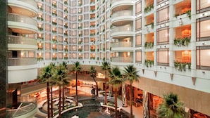 Interior de hotel de varios niveles con balcones, plantas de interior y un atrium central con palmeras.