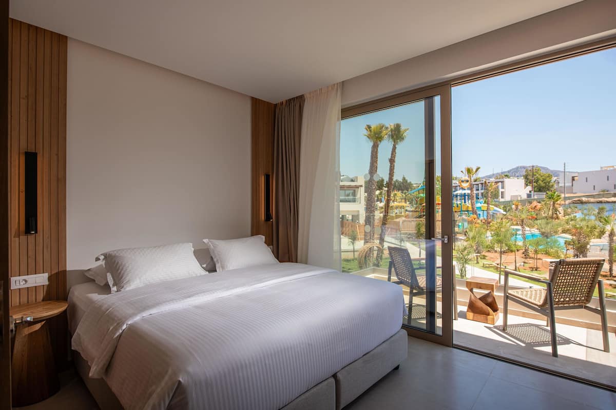 A hotel room with a large bed, a wooden nightstand, a glass door leading to a balcony with a pool view.