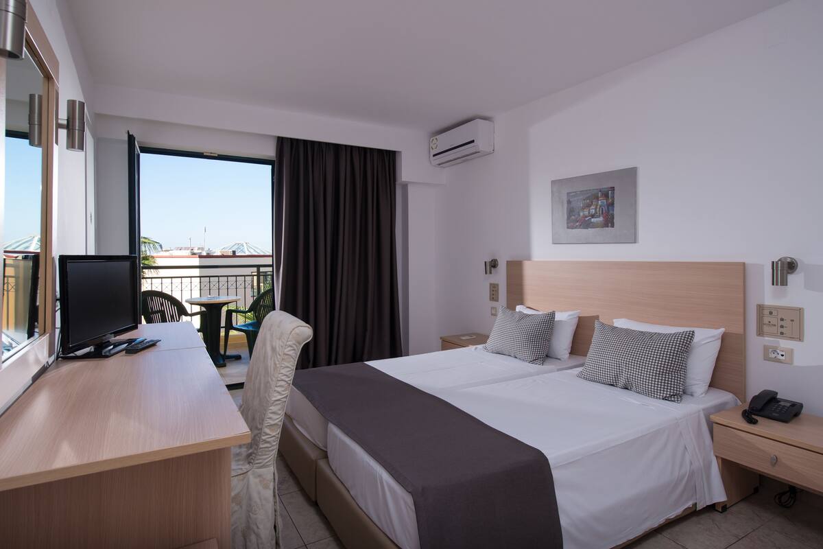 A hotel room with a bed, bedside tables, a desk with a computer, a chair, and a view of the outside.