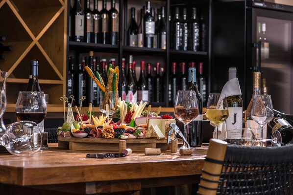 A bar area with a wooden counter, various bottles of wine, glasses, and a charcuterie board with cheeses and fruits. - Gouves Water Park Holiday Resort (Hersonissos)