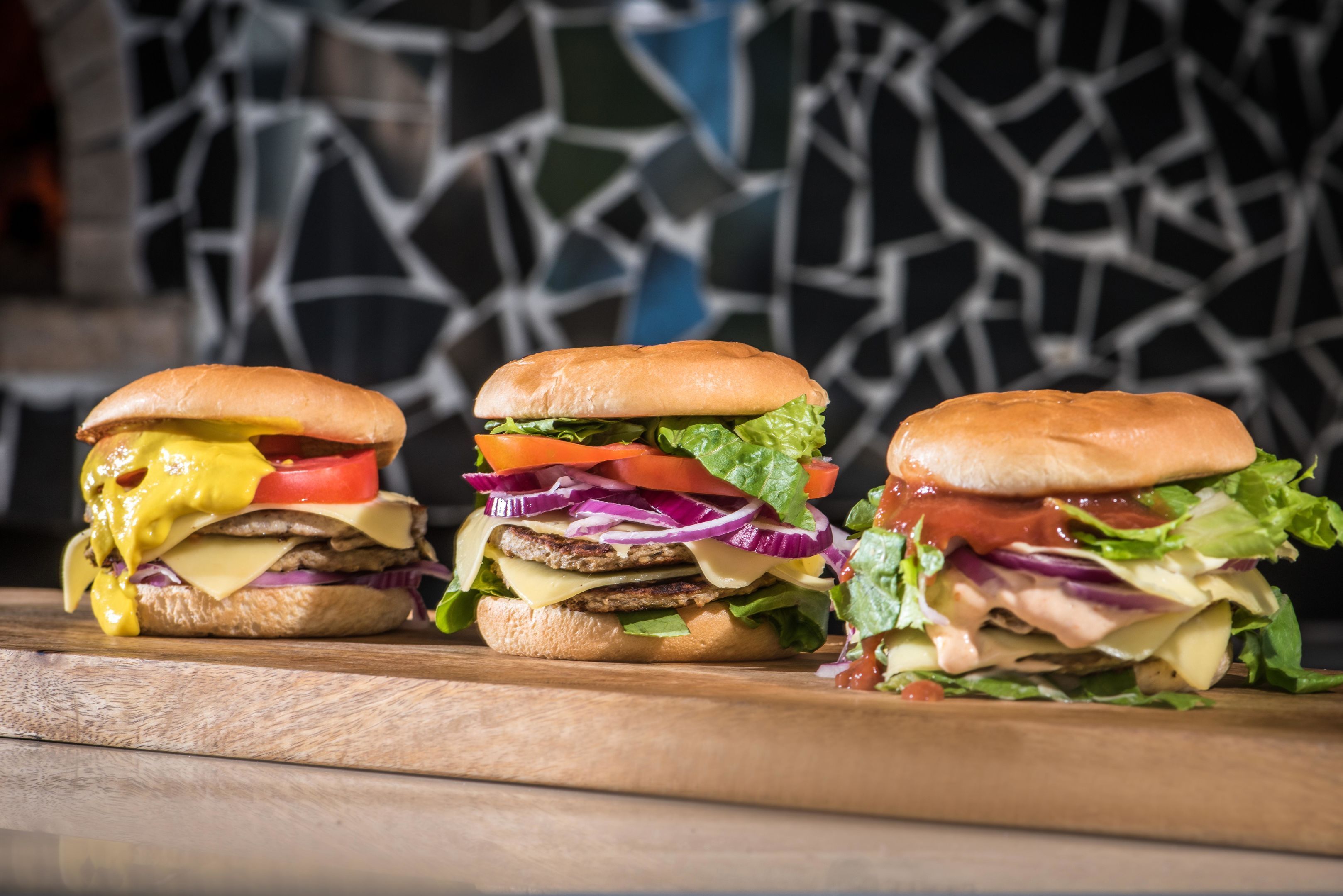 Drie burgers op een houten oppervlak, met een gescheurde muur op de achtergrond.