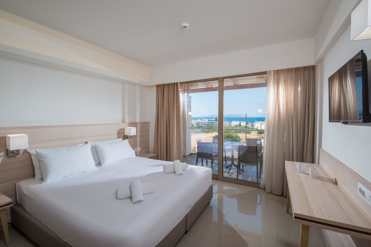 A hotel room with a large bed, a desk, and a balcony with a view.