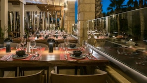 A restaurant with multiple tables set for dining, featuring a view of palm trees and a clear sky. - Gouves Water Park Holiday Resort (Hersonissos)