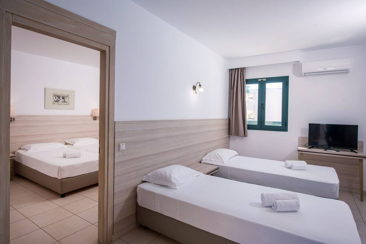 A hotel room with two beds, a television, an air conditioner, and a window with curtains.