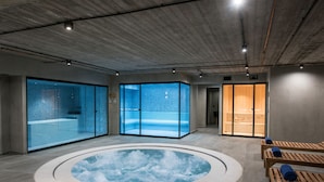 A spa area with a hot tub, wooden loungers, and glass-enclosed saunas. - Gouves Water Park Holiday Resort (Hersonissos)