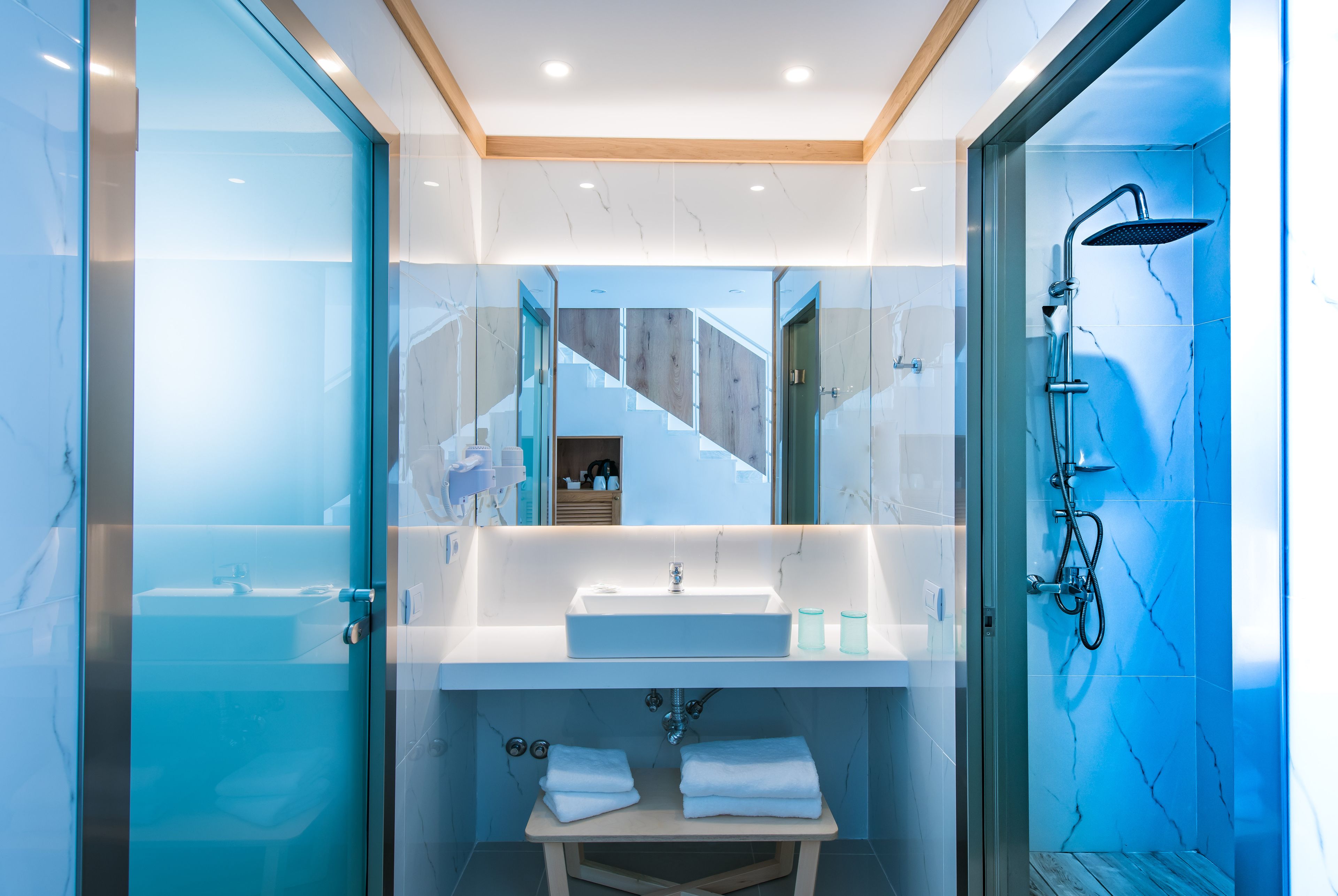 A modern bathroom with a glass-enclosed shower, a white sink, and a wooden bench.