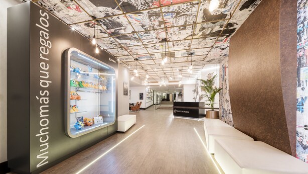 A modern hotel lobby with a clear glass display case filled with plush toys, a reception desk, and a ceiling with a unique, artistic design. - Hotel ILUNION Bilbao (Bilbao)
