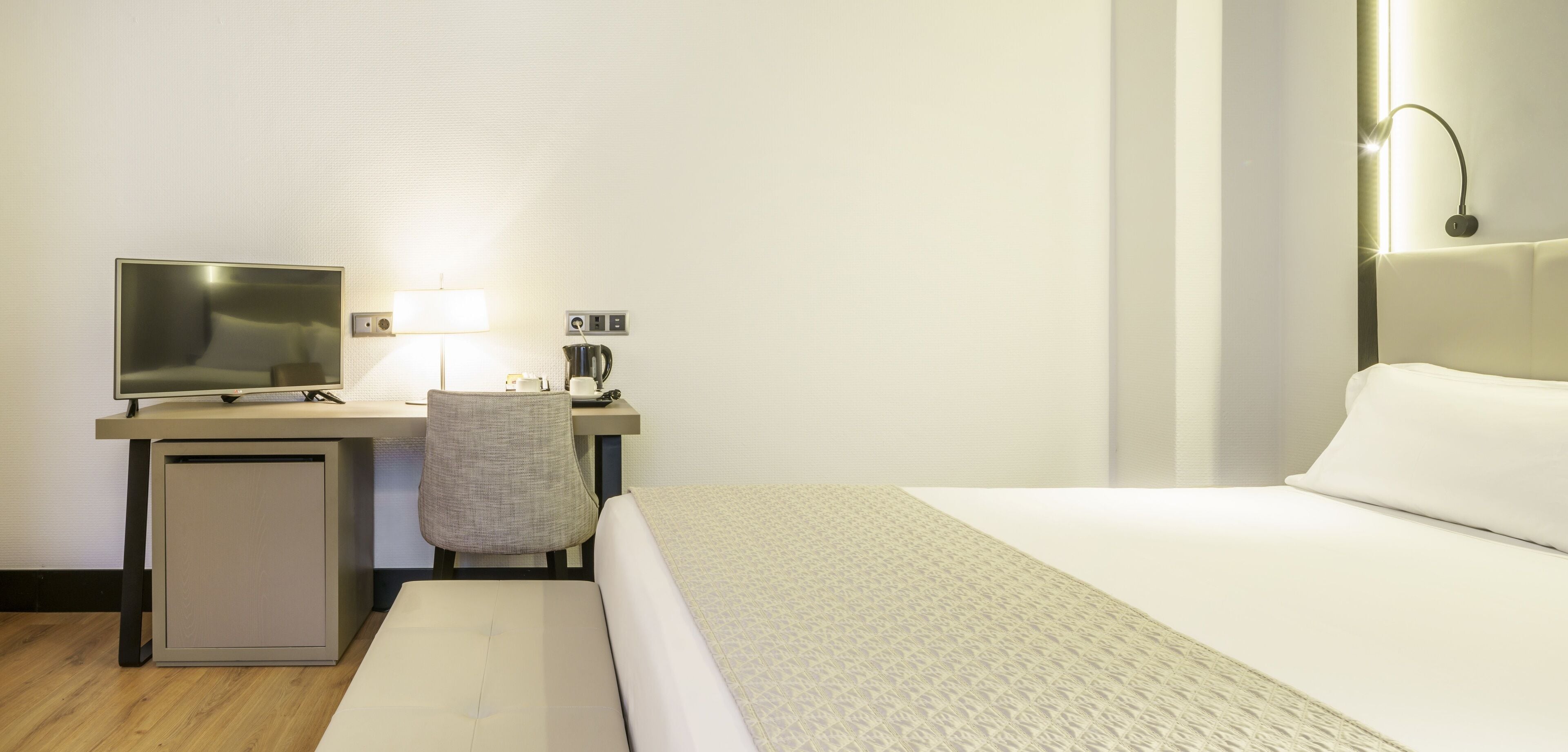 Una habitación de hotel con una cama, un escritorio con computadora, una silla y un mueble bajo.