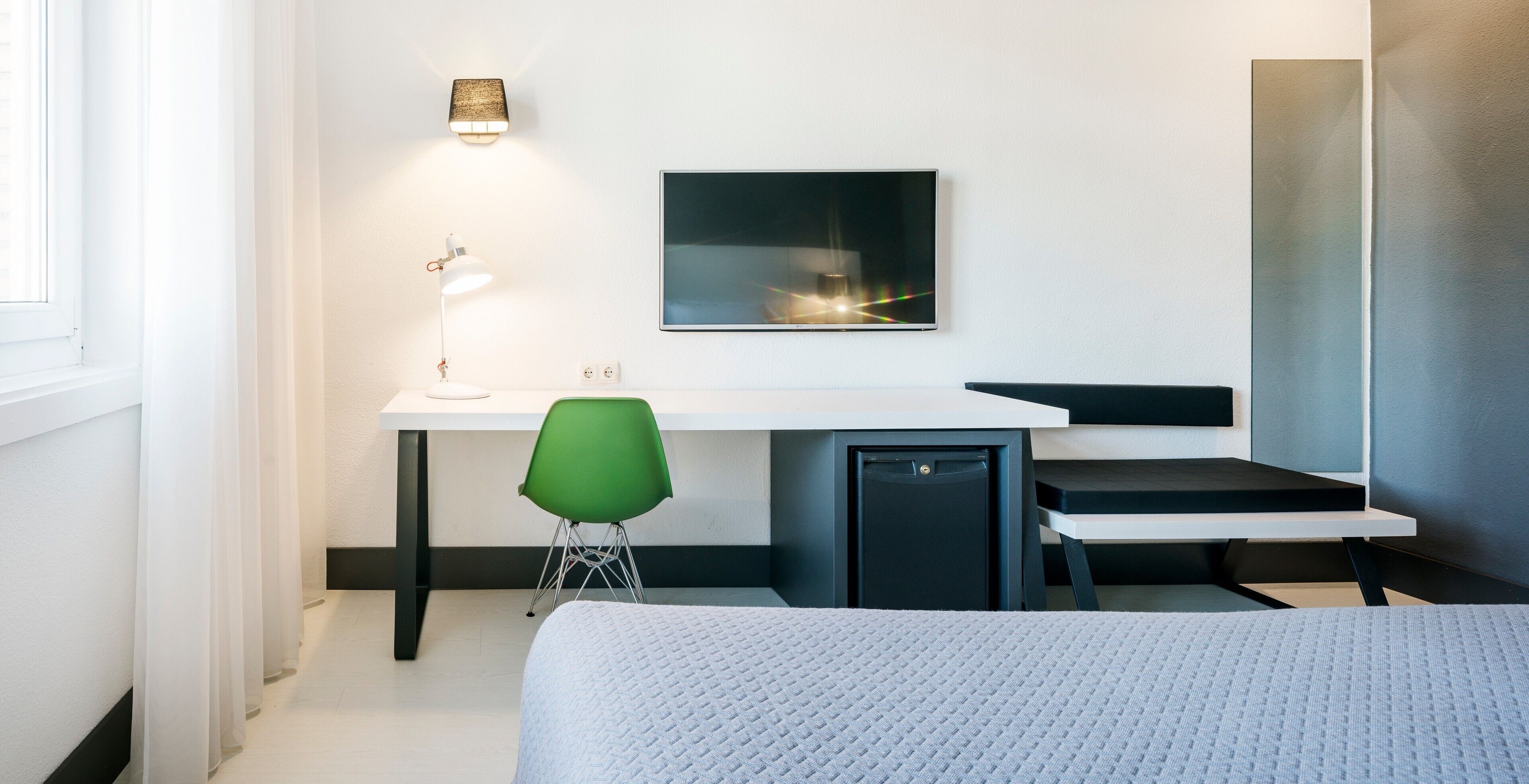 Ein modernes Schlafzimmer mit Bett, Schreibtisch, Stuhl und Fernseher.