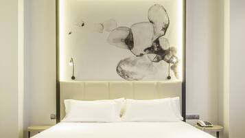Una habitación de hotel moderna con una cama grande, cabecera con panel de luz y una obra de arte abstracto colgada en la pared.