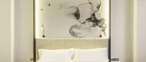 A modern hotel room with a large bed, a headboard with a light panel, and a wall-mounted abstract art piece.