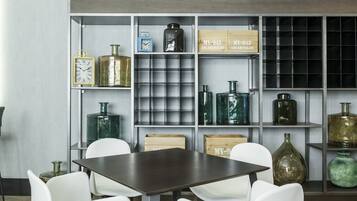 Un interior moderno con una mesa de madera oscura y sillas blancas, rodeado de estanterías con varias botellas de vidrio y cajas de madera con la etiqueta 'MY-943'.