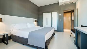 Una habitación de hotel moderna con una cama grande, mesitas de noche, un escritorio y un espejo.