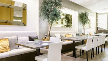 Un comedor moderno con una larga mesa, asientos blancos acolchados y plantas en macetas.