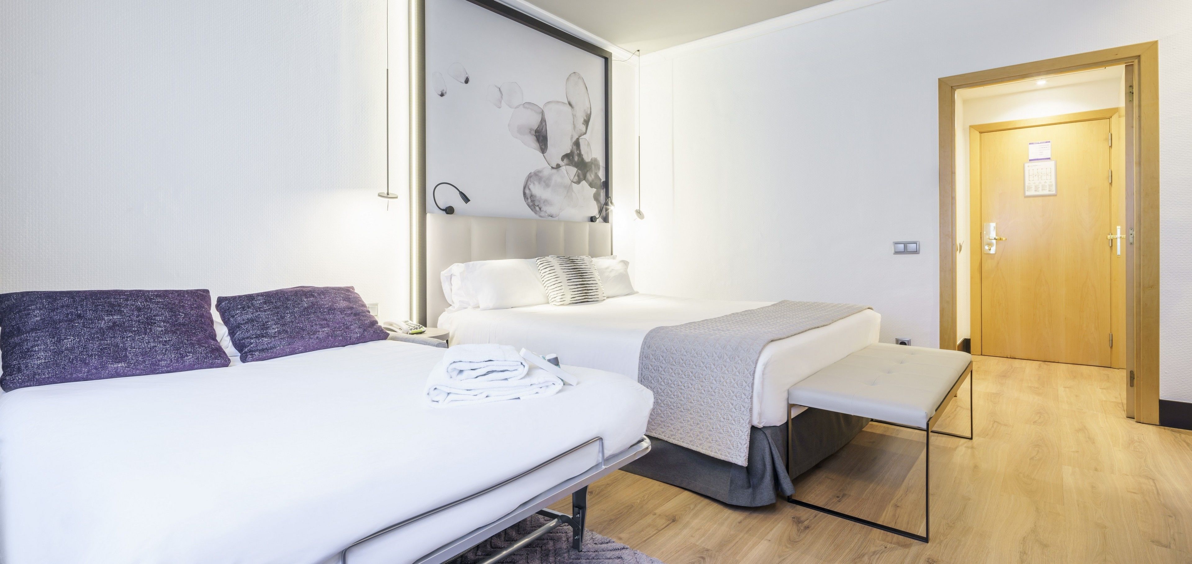 Une chambre d’hôtel avec deux lits, une table de chevet, une œuvre d’art accrochée au mur et une porte en bois.