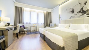 A hotel room with a bed, two chairs, a desk, a small table, and a large abstract painting on the wall. - Hotel ILUNION Bilbao (Bilbao)