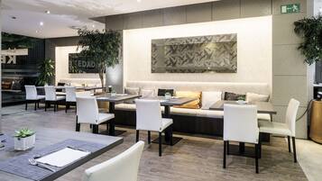 Ein modernes Restaurant mit Sitzbereich, der Tische und Stühle, ein großes Wandbild und Topfpflanzen umfasst.
