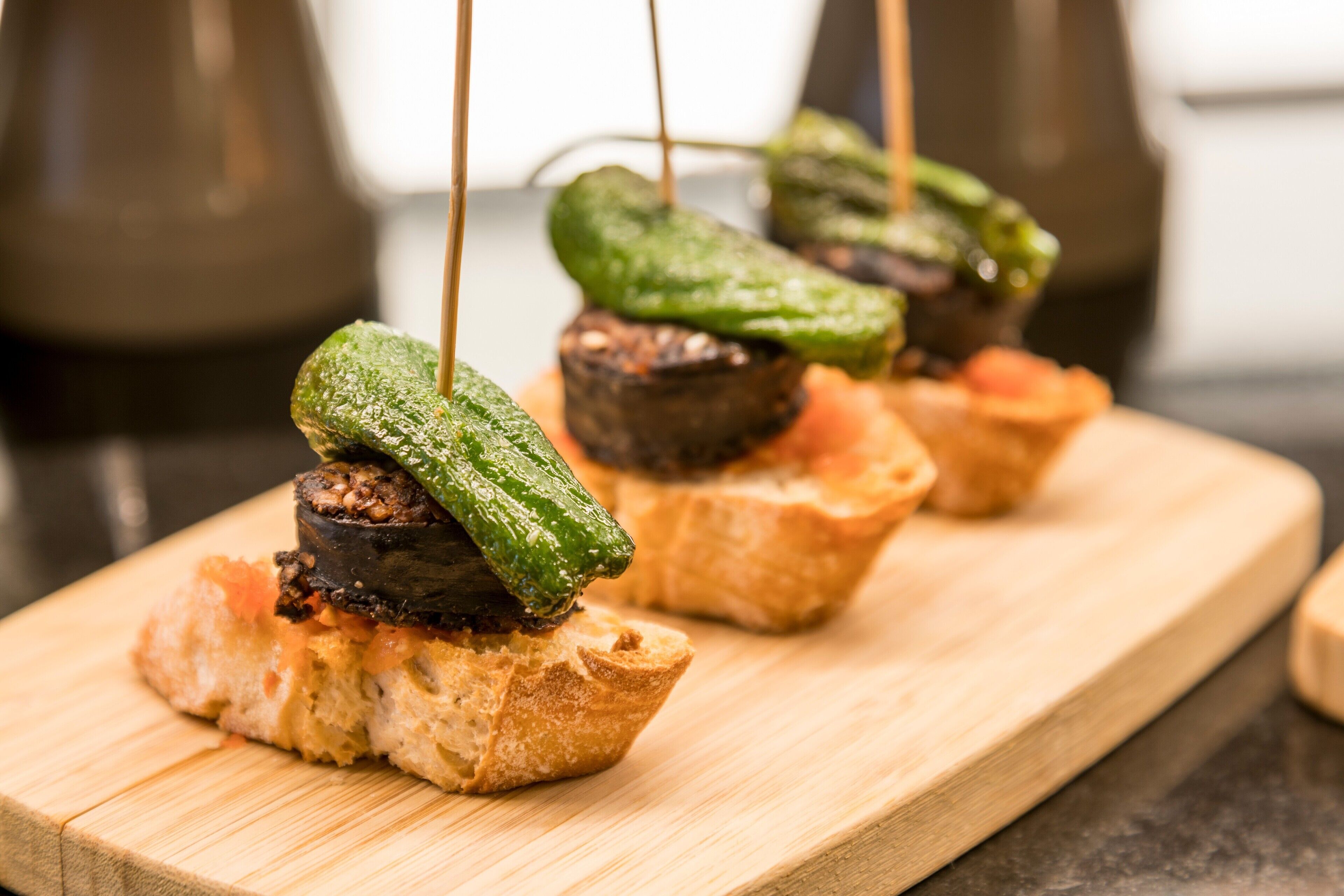 A wooden board with food items, including a piece of bread topped with a grilled vegetable and a small piece of meat.