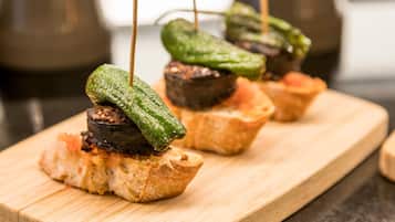 Una tabla de madera con alimentos, entre ellos una rebanada de pan cubierta con un vegetal a la parrilla y un trozo pequeño de carne.