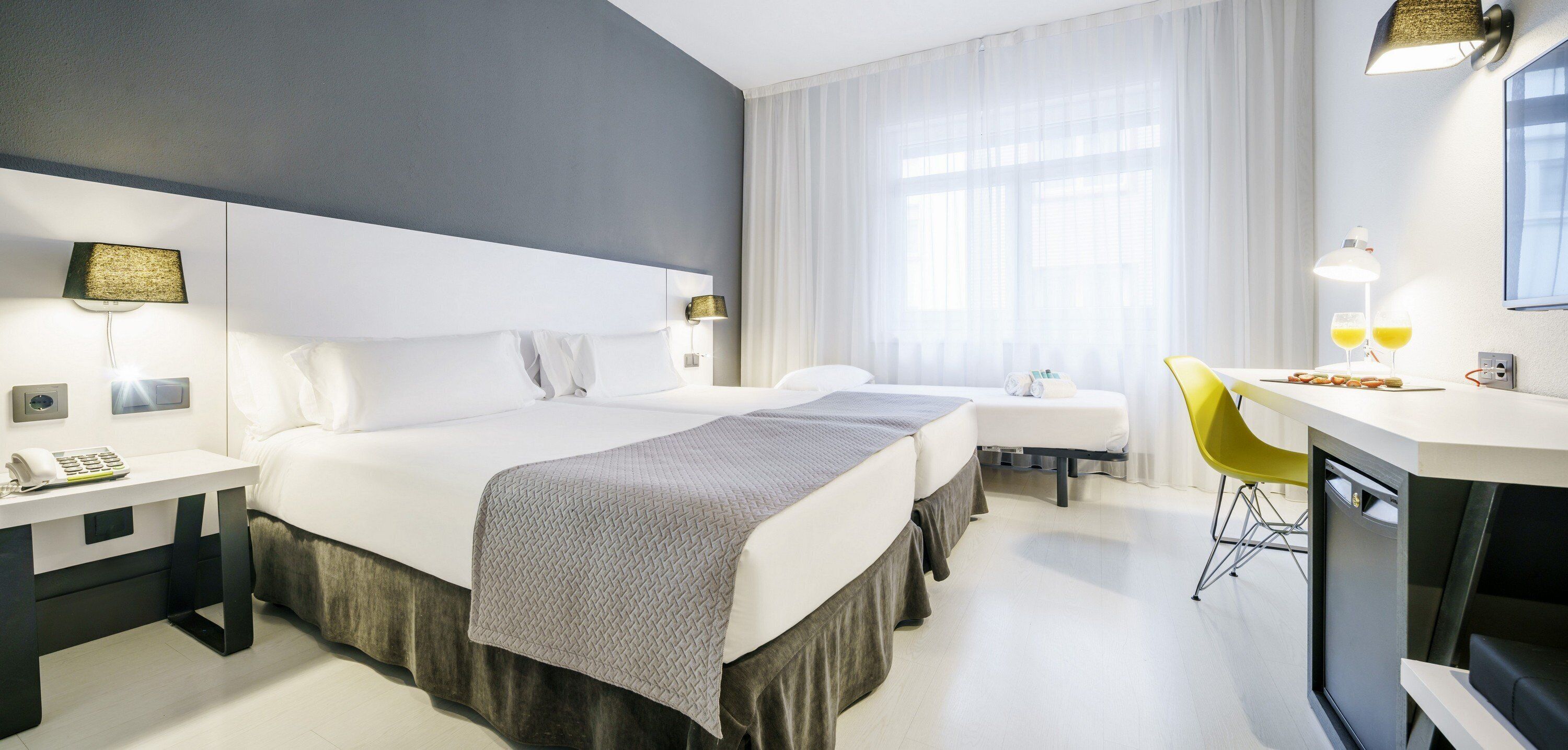 Una habitación de hotel con una cama grande, mesitas de noche, un escritorio con una silla y una ventana con cortinas.