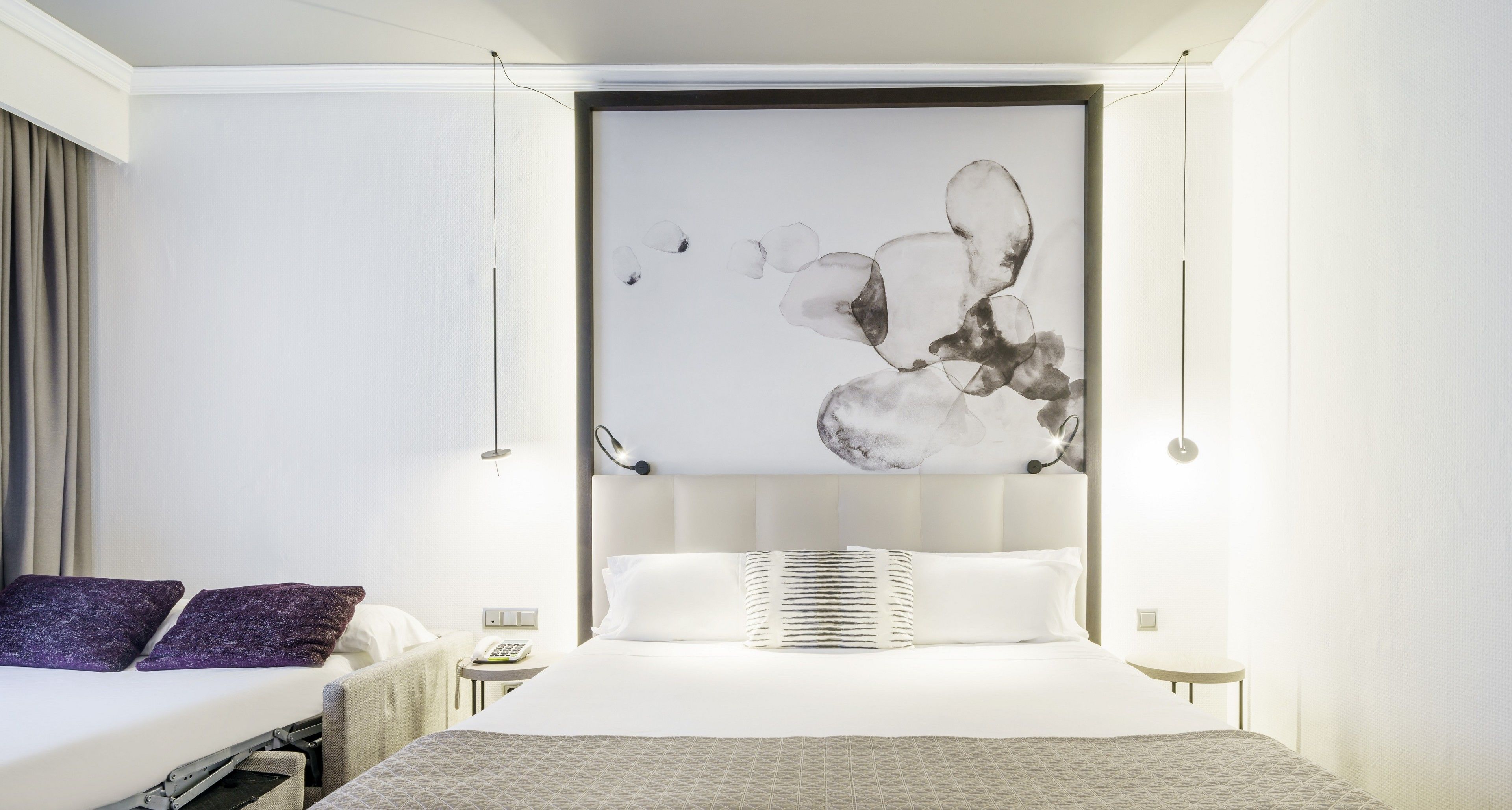 Una habitación de hotel moderna con una cama grande, una mesita de noche con lámpara y una obra de arte colgada en la pared.