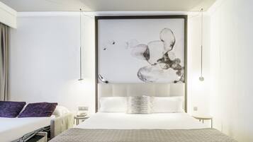 Una habitación de hotel moderna con una cama grande, una mesita de noche con lámpara y una obra de arte colgada en la pared.