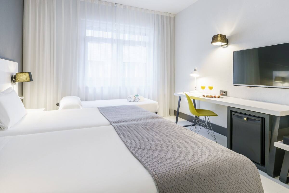 A hotel room with two beds, a desk, a chair, a television, and a minibar.