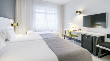 Una camera d'albergo con due letti, una scrivania, una sedia, un televisore e un frigobar.