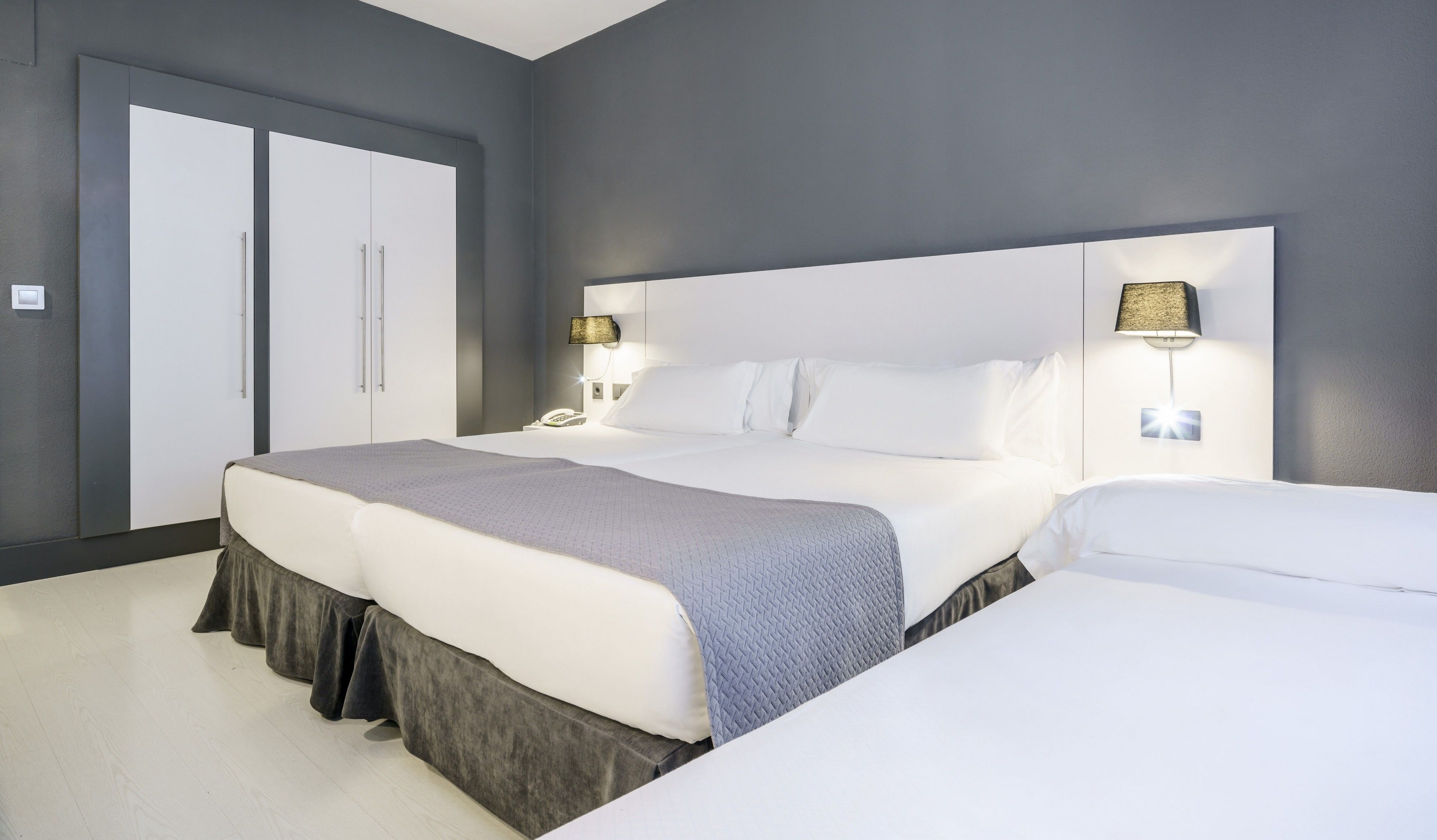 Une chambre d’hôtel avec un grand lit, des tables de chevet, une armoire et des lampes fixées au mur.