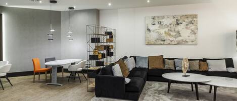 A modern living room with a sectional sofa, a round coffee table, and a dining area with a white table and orange chairs.