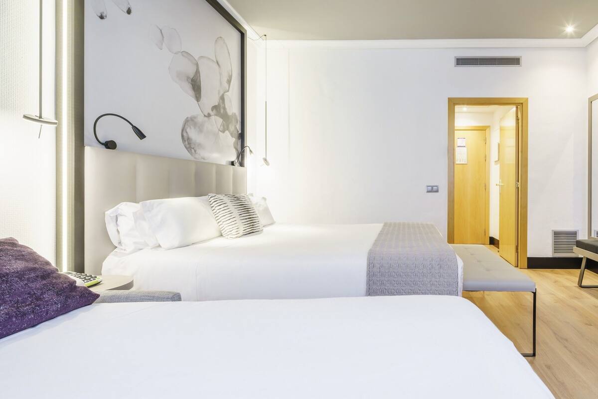 A hotel room with two beds, a desk, a chair, a TV, and a bathroom visible through an open door.